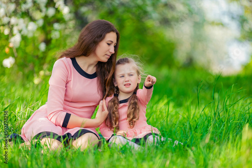 mother and daughter sit in the green grass against the backdrop of blooming apple trees © zokov_111