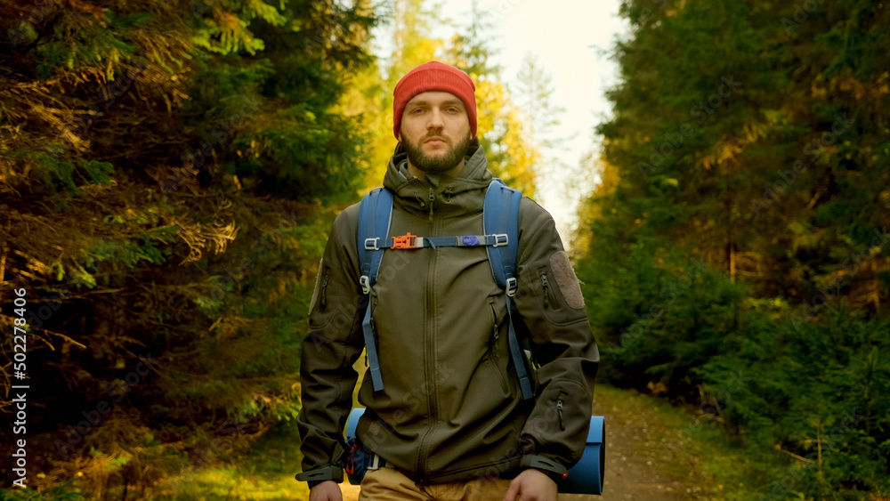 Portrait Active Healthy Caucasian Tourist With Backpack Walking in sunshine Wood. Male Traveler With Walks Along Forest, Leisure, bio-tourism. Young Man Hiking in Forest in Autumn.