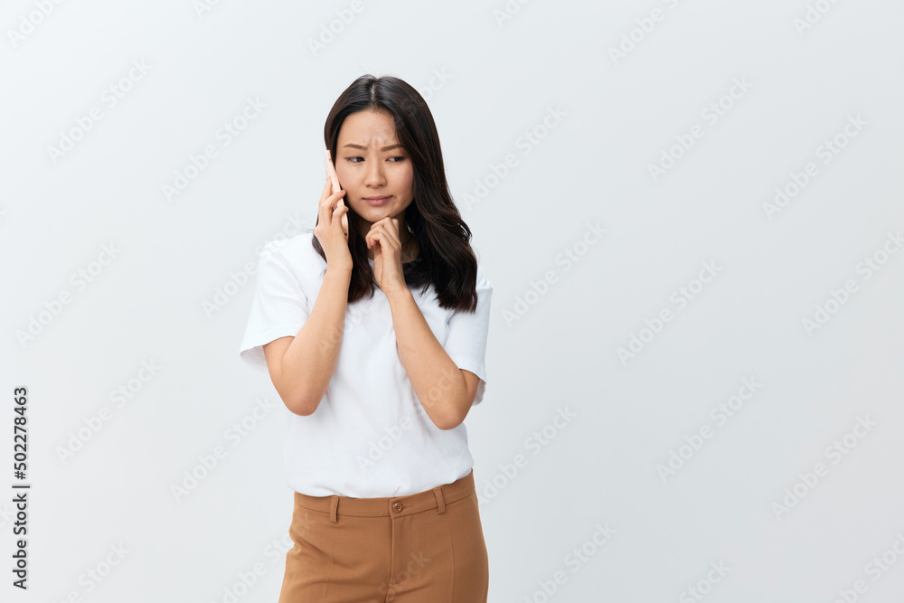 Thoughtful cute Asian young female in white basic t-shirt get important info in call from director using phone posing isolated on over white background. The best offer for ad. People Lifestyle concept Thoughtful cute Asian young female in white basic t-shirt get important info in call from director using phone posing isolated on over white background. The best offer for ad. People Lifestyle concept