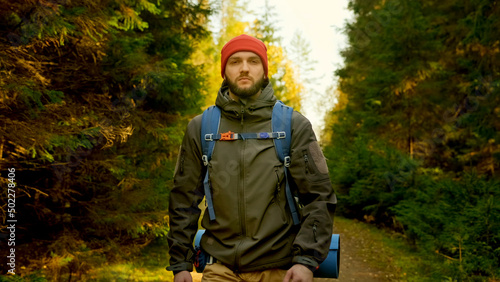 Portrait Active Healthy Caucasian Tourist With Backpack Walking in sunshine Wood. Male Traveler With Walks Along Forest, Leisure, bio-tourism. Young Man Hiking in Forest in Autumn. © orientka