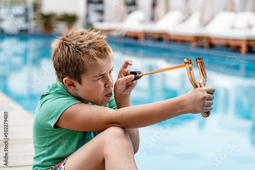 A boy shoots a slingshot near the pool