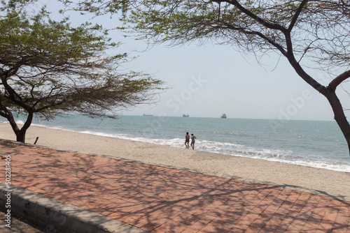 Two women walking in Santa Marta, Colombia airport beach with caribbean sea and big ships at background
