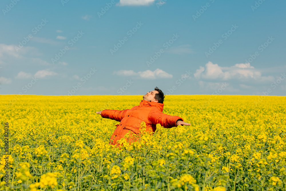 Fototapeta premium Stylish man in orange jacket in rapeseed field
