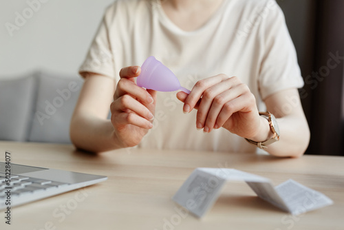 Minimal close up of young woman holding menstrual cup with instruction manual in foreground, copy space photo