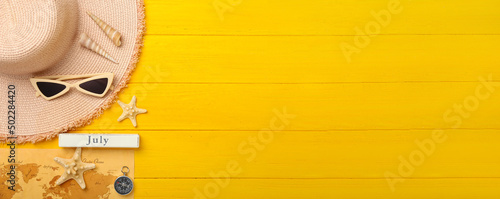 Beach accessories, map and compass on yellow wooden background with space for text photo