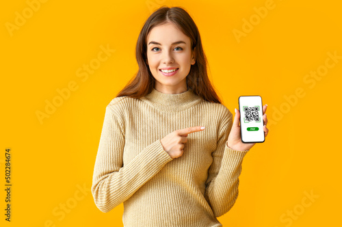 Fotografie Beautiful young woman holding smartphone with QR code on screen against orange b