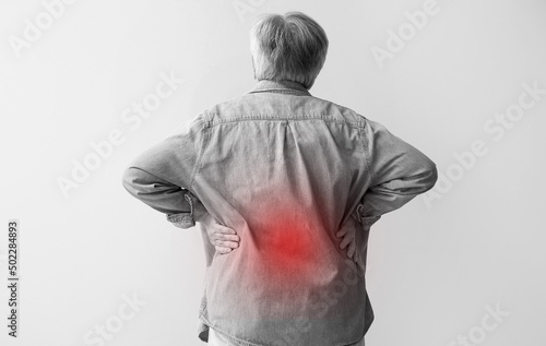 Senior woman suffering from back pain on light background