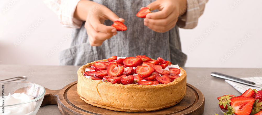 Woman decorating tasty pie with strawberry at table in kitchen
