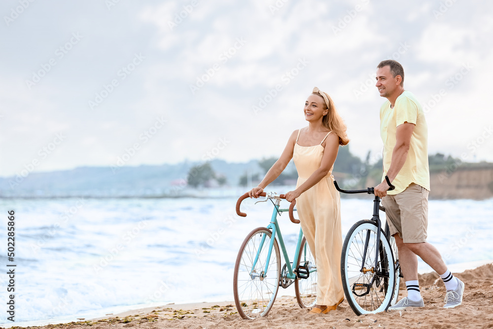 Fototapeta premium Mature couple with bicycles walking along sea beach on summer day