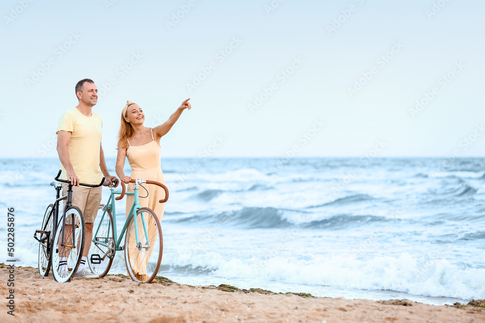 Mature couple with bicycles walking along sea beach on summer day Mature couple with bicycles walking along sea beach on summer day