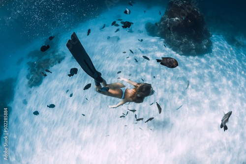 Woman freediver dive with fins over sandy bottom with fish.