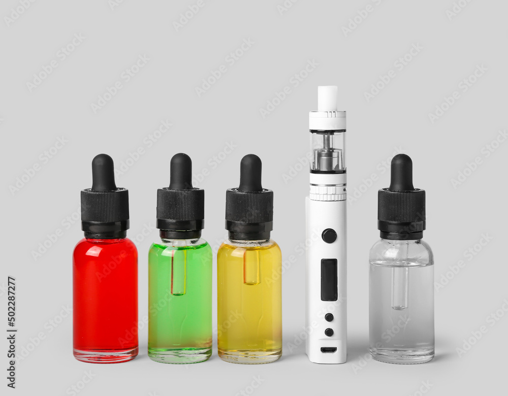 Modern vape mod and oils on light background Modern vape mod and oils on light background