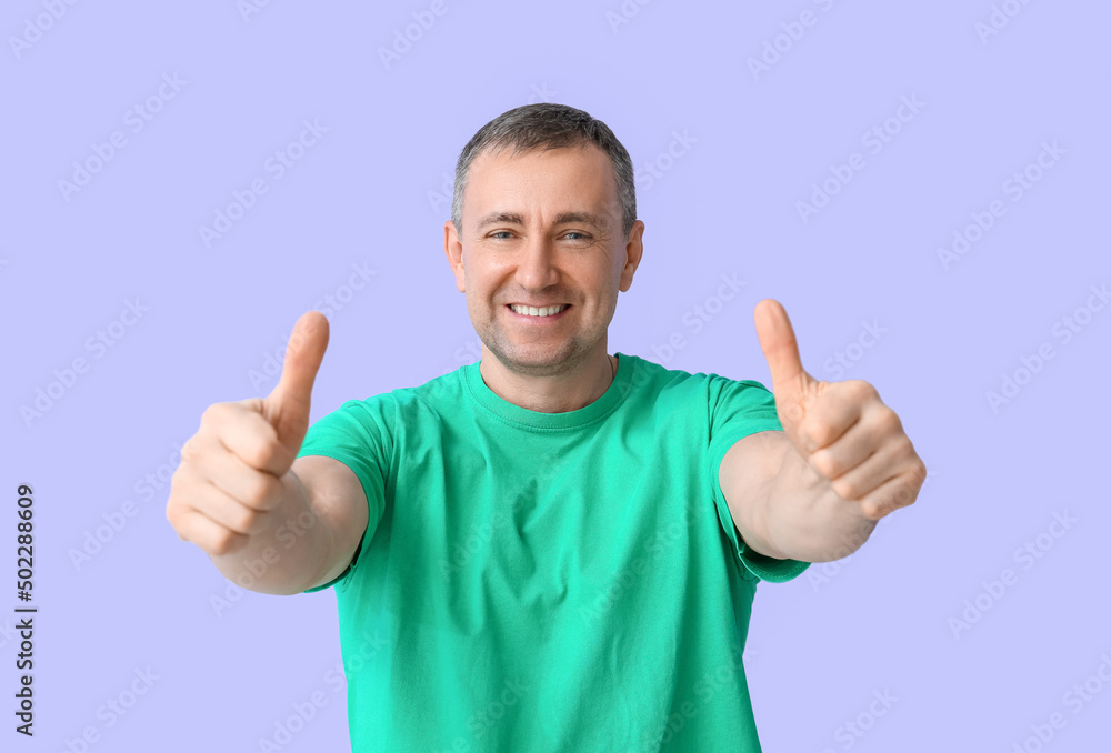 Mature man in green t-shirt showing thumbs-up on lilac background Mature man in green t-shirt showing thumbs-up on lilac background