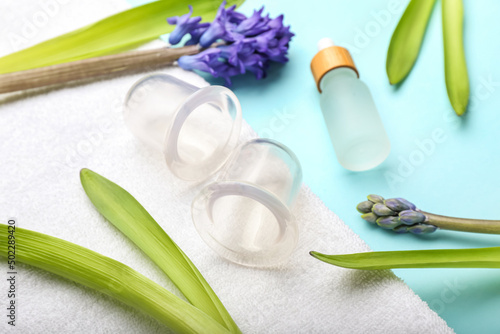 Composition with vacuum jars for anti-cellulite massage, bottle of essential oil, towel and flowers on color background