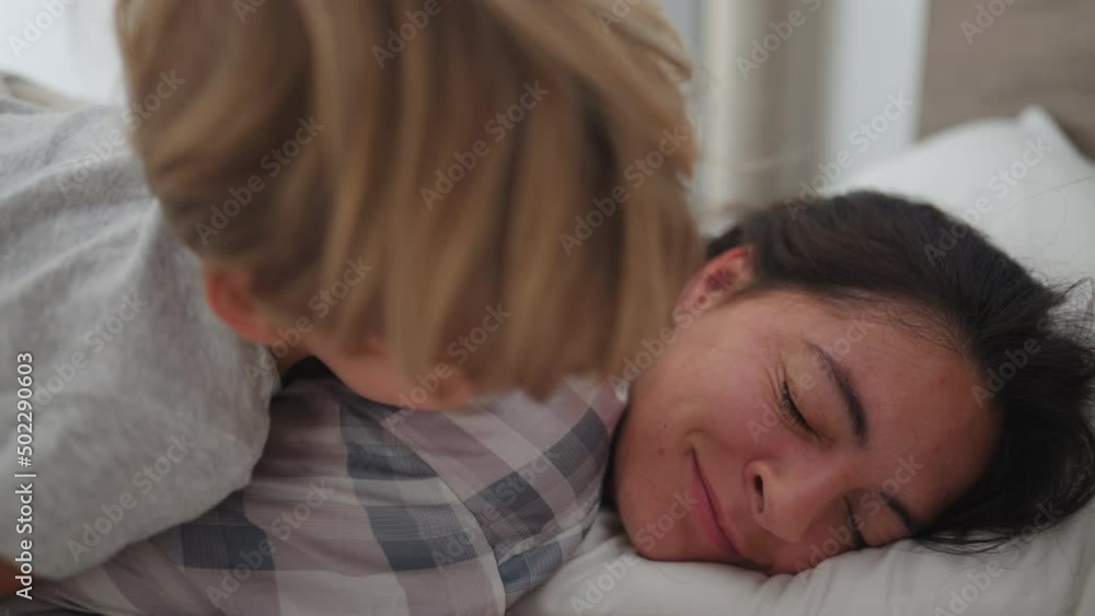 Little boy waking up mother in the morning jumping into mom and kissing Little boy waking up mother in the morning jumping into mom and kissing