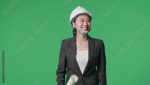 Smiling Asian Female Engineer With Blueprint Looking Around And Shaking Her Head While Walking In The Green Screen Studio
 photo