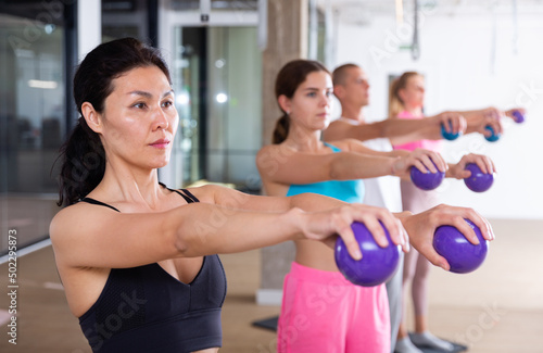 Group of active people engaged in fitness in the studio perform various exercises  holding special small Pilates balls in ..their hands