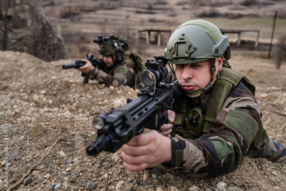 Two men soldiers holding position in the battle war zone aiming rifles dogs of war professional mercenaries or volunteers special forces on a mission attacking or defending enemy copy space Two men soldiers holding position in the battle war zone aiming rifles dogs of war professional mercenaries or volunteers special forces on a mission attacking or defending enemy copy space