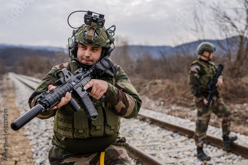 Two soldiers dogs of war mercenaries men in uniform armed service rifles aiming gun while securing the railroad in combat zone in war military battle observing territory patrolling area during mission photo