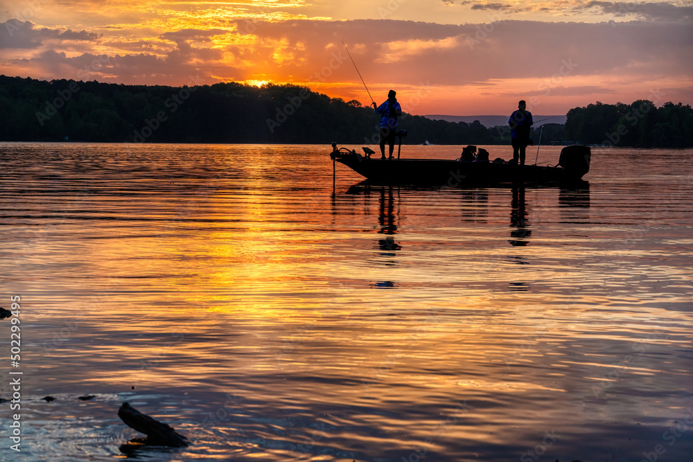 Two men bass fishing in a bass boat on Tims Ford lake in Tennessee with  early morning sunrise silhouette. Stock Photo
