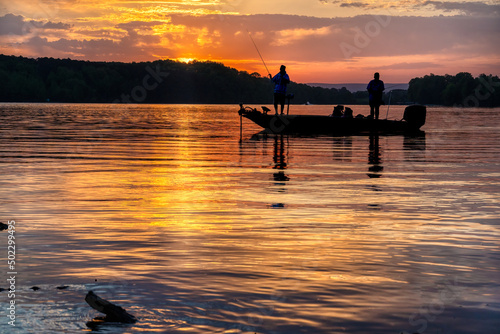 Two men bass fishing in a bass boat on Tims Ford lake in Tennessee with early morning sunrise silhouette.