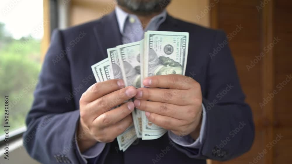 Man with dark coat counting $100 bills Man with dark coat counting $100 bills
