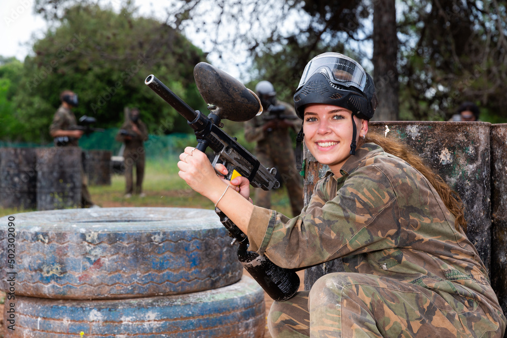Fototapeta premium Paintball players of one team in camouflages and masks aiming with gun in shootout playing field