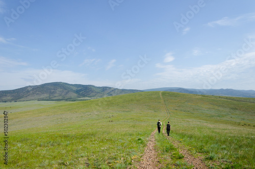 Two travelers walk along the road among the green hills. Hiking in nature.