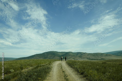 A sunny summer day. Two people walk along the trail towards the mountains.