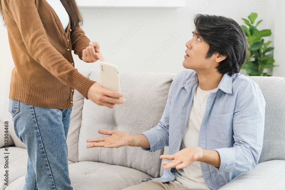 Infidelity, suspicion asian young couple love fight relationship, wife holding cellphone, smartphone cheating on phone, scolding husband about mistrust, distrust and jealousy when sitting at home. Infidelity, suspicion asian young couple love fight relationship, wife holding cellphone, smartphone cheating on phone, scolding husband about mistrust, distrust and jealousy when sitting at home.