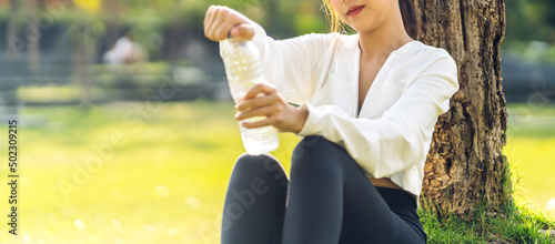 Portrait sport asian beauty body slim woman drinking water from a bottle while relax and feeling fresh on green natural background at summer green park.Healthy lifestyle concept