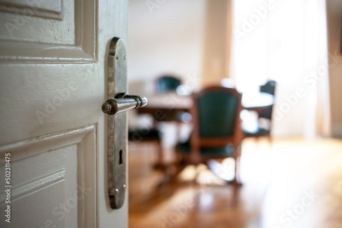 Door open close up. Retro doorknob on white door, blur floor parquet, classy house interior