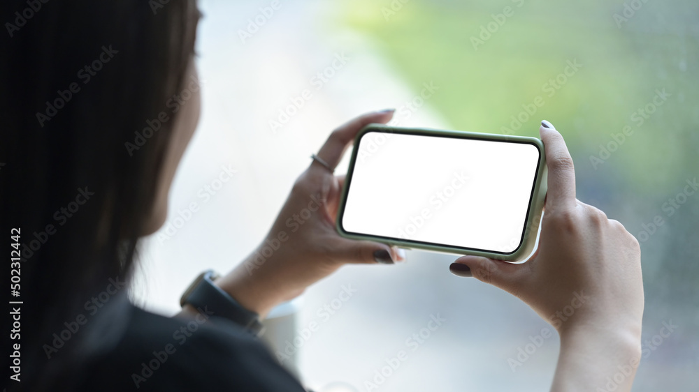 View over shoulder of young woman holding smart phone in horizontal position. Empty screen for advertising text.