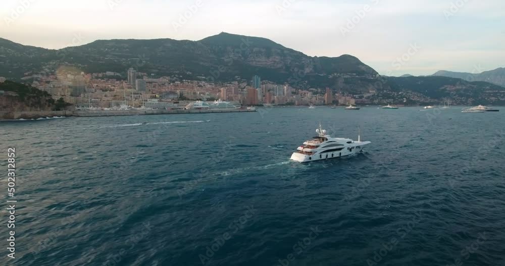 Aerial Shot Of White Nautical Vessels At Harbor By City, Drone Flying Backwards Over Sea Waves - Monaco Aerial Shot Of White Nautical Vessels At Harbor By City, Drone Flying Backwards Over Sea Waves - Monaco