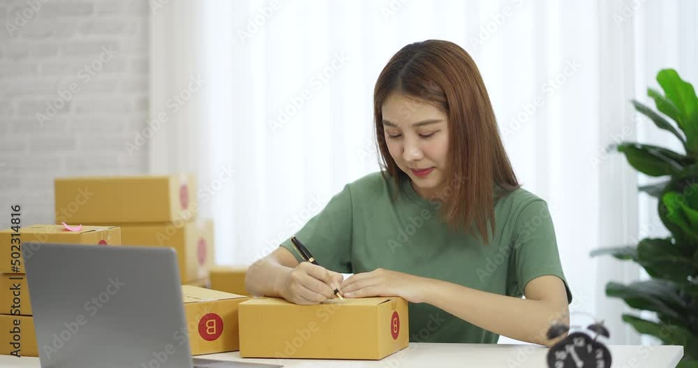 Happy young Asian business owner woman prepare parcel box and check online orders of product for deliver to customer on laptop computer. Shopping Online concept. Happy young Asian business owner woman prepare parcel box and check online orders of product for deliver to customer on laptop computer. Shopping Online concept.