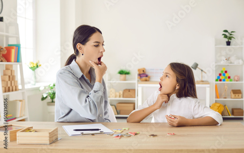 Photos Happy child and young female speech therapist or mother doing mouth exercise, wo
