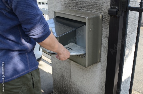 男性が郵便ポストから新聞を取り出しています。
