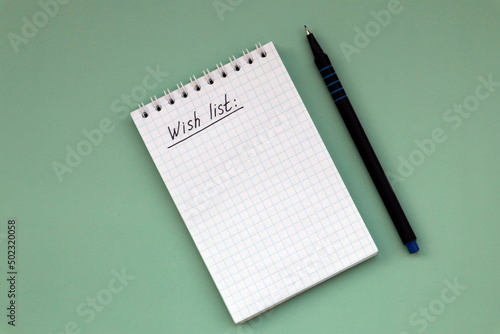 Notebook with wish list on green background and pen with copy space.