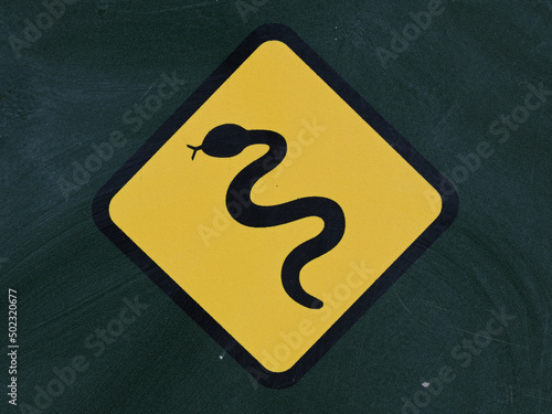 Close up of a black snake icon, in a yellow diamond, on a dark green sign to warn people about the presence of snakes in the area