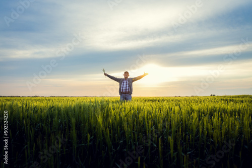 Portrait of senior farmer standing in barley field with his outstretched arms at sunset.