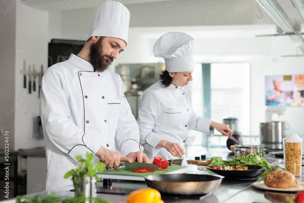 Skilled and confident head chef chopping organic and fresh red bell pepper while preparing garnish. Food industry worker cooking delicious gourmet dish for dinner service at restaurant.