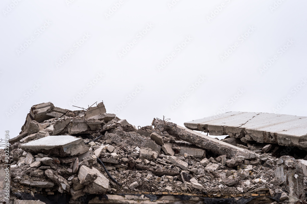 The remains of a destroyed building in the form of a pile of gray concrete debris and construction debris against a gray sky. Background