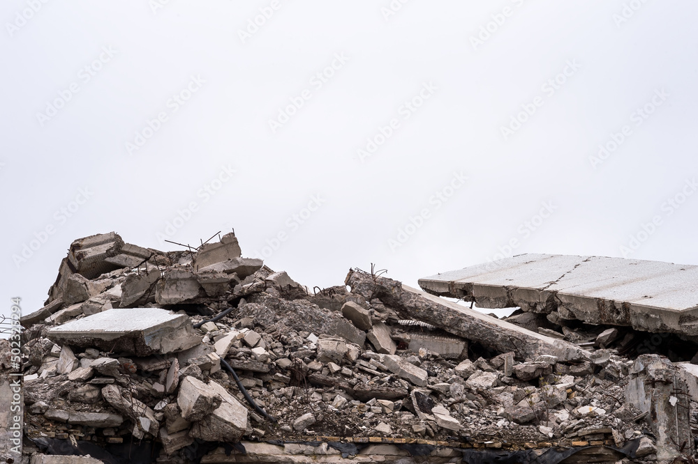 The remains of a destroyed building in the form of a pile of gray concrete debris and construction debris against a gray sky. Background The remains of a destroyed building in the form of a pile of gray concrete debris and construction debris against a gray sky. Background