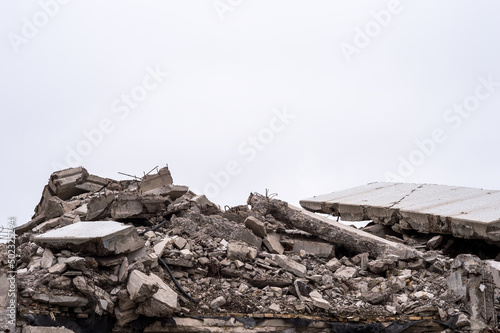 The remains of a destroyed building in the form of a pile of gray concrete debris and construction debris against a gray sky. Background