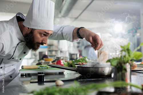 Food industry worker preparing ingredients for meal while seasoning vegetable stew with herbs and spices. Culinary expert seasoning food while cooking gourmet dish served in fine dining restaurant.