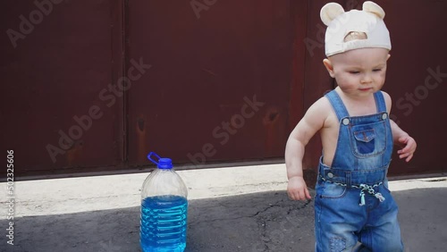 Baby mechanic stands next to bottle of antifreeze, then moves out of frame. In background in frame are auto parts