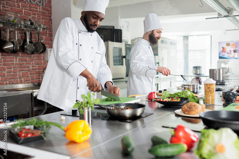 Food industry african american worker chopping fresh organic herbs while cooking gourmet dish. Head chef in preparation process of dinner meal in restaurant professional kitchen. Food industry african american worker chopping fresh organic herbs while cooking gourmet dish. Head chef in preparation process of dinner meal in restaurant professional kitchen.
