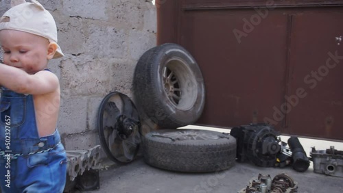 Serious little mechanic walks with wrench and walks out of frame. Auto parts in background