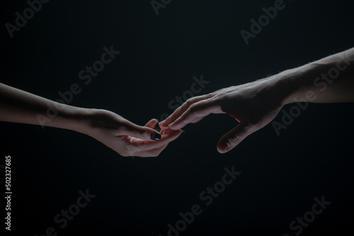 Two hands stretch each other, black background. Couple in love holding hads, close up. Helping hand, support, friendship.