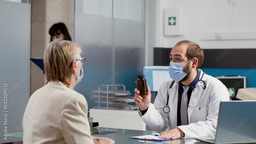 General practitioner giving prescription medicine in bottle to elder patient with disease, attending checkup appointment during pandemic. Senior woman receiving treatment from medic. General practitioner giving prescription medicine in bottle to elder patient with disease, attending checkup appointment during pandemic. Senior woman receiving treatment from medic.
